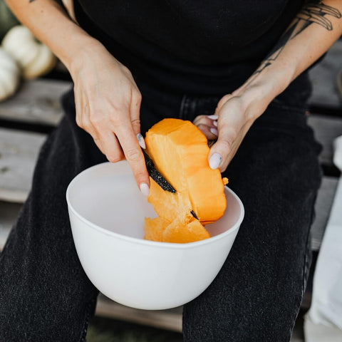 A dog owner wearing a black t-shirt and jeans is actively dicing a bright orange pumpkin, highlighting the preparation of pumpkin which offers numerous benefits for dogs