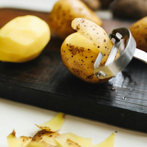 A potato being peeled on a wooden cutting board, raising the question Does My Dog Need Carbohydrates